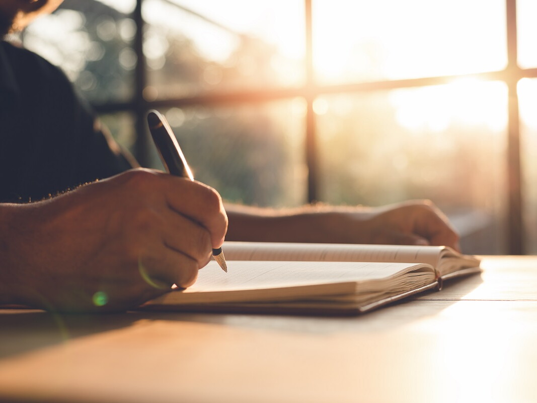 Hand schreibt in Notizbuch bei Sonnenschein
