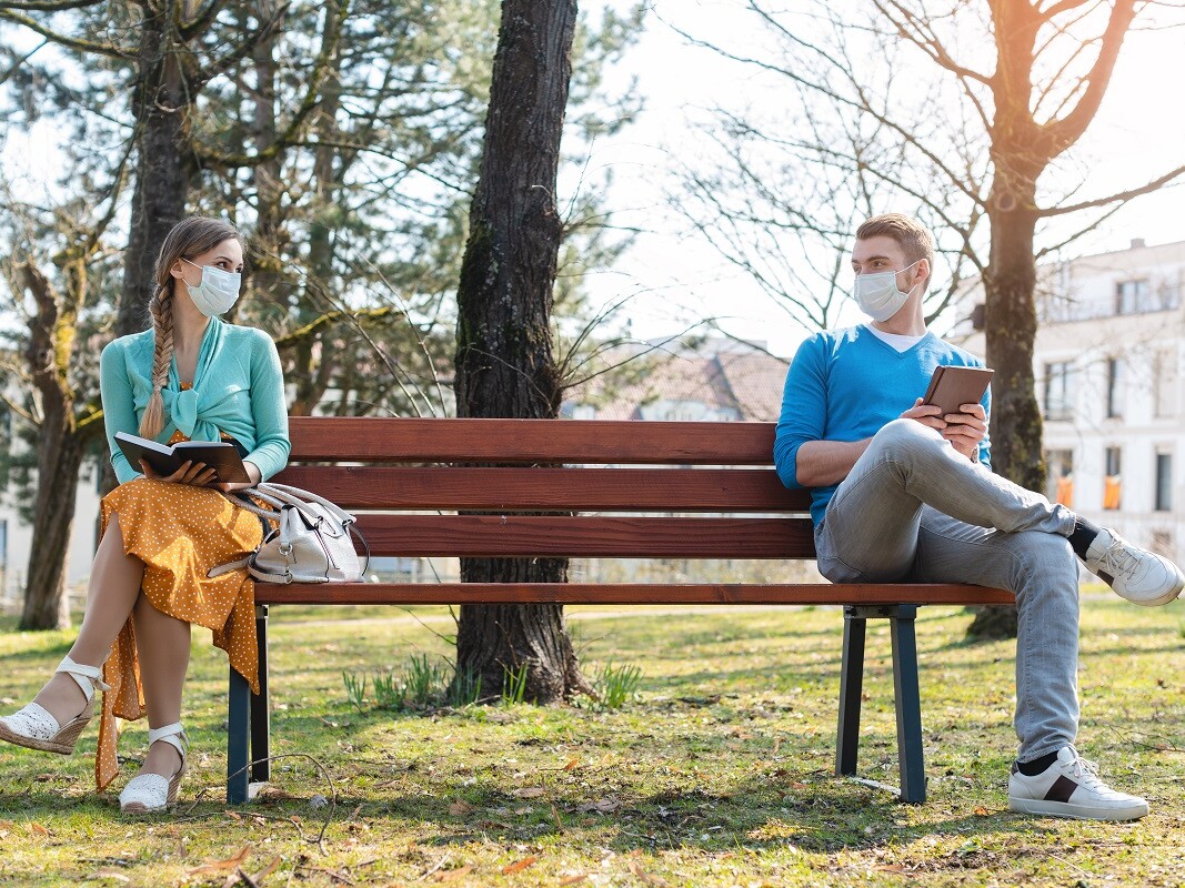 Mann und Frau auf Parkbank mit medizinischen Masken
