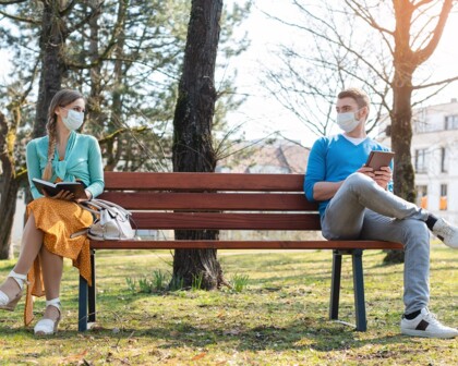 Mann und Frau auf Parkbank mit medizinischen Masken