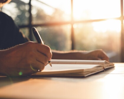 Hand schreibt in Notizbuch bei Sonnenschein